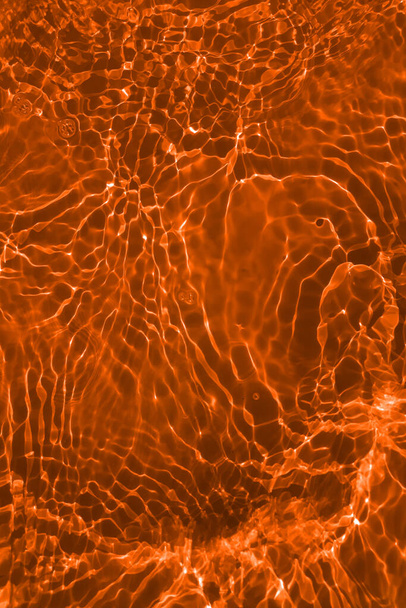 Defocus θολή διάφανη πορτοκαλί χρώμα διαυγή ήρεμη επιφάνεια του νερού υφή με πιτσιλιές και φυσαλίδες. Μοντέρνο αφηρημένο φόντο της φύσης. Κύματα νερού στο φως του ήλιου με αντιγραφή χώρου. Πορτοκαλί νερό λάμπει - Φωτογραφία, εικόνα