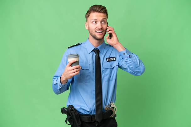 Giovane poliziotto su sfondo isolato in possesso di caffè da portare via e un cellulare - Foto, immagini