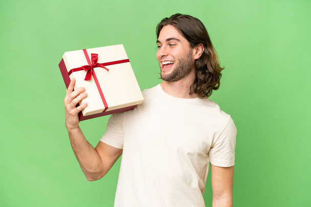 Młody przystojny mężczyzna trzyma dar na odosobnionym tle ze szczęśliwym wyrazem twarzy - Zdjęcie, obraz