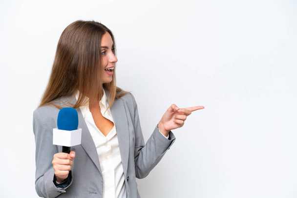 Jovem apresentadora de TV mulher caucasiana isolado no fundo branco apontando o dedo para o lado e apresentando um produto - Foto, Imagem