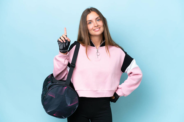 Young sport woman with sport bag isolated on blue background showing and lifting a finger in sign of the best - Фото, изображение