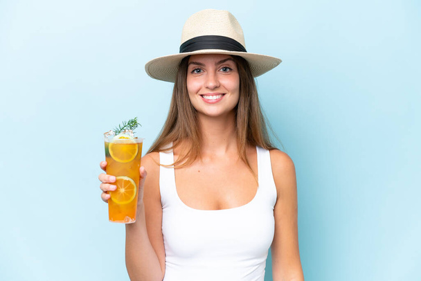 Junge schöne Frau hält einen Cocktail isoliert auf blauem Hintergrund und lächelt viel - Foto, Bild