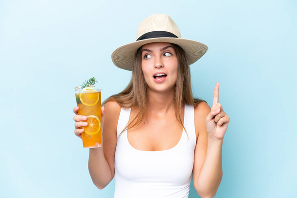 Junge schöne Frau hält einen auf blauem Hintergrund isolierten Cocktail in der Absicht, die Lösung zu erkennen, während sie den Finger hebt - Foto, Bild