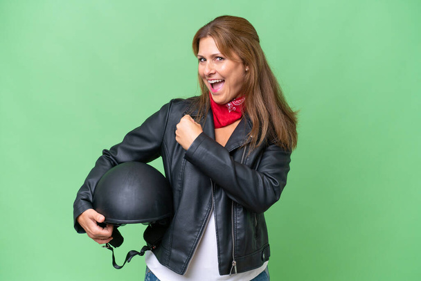 Mulher caucasiana de meia-idade com um capacete de motocicleta sobre fundo isolado celebrando uma vitória - Foto, Imagem