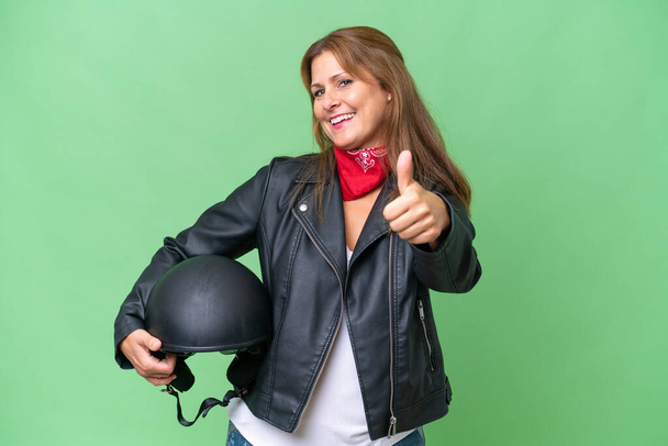 Middle-aged caucasian woman with a motorcycle helmet over isolated background with thumbs up because something good has happened - Photo, Image