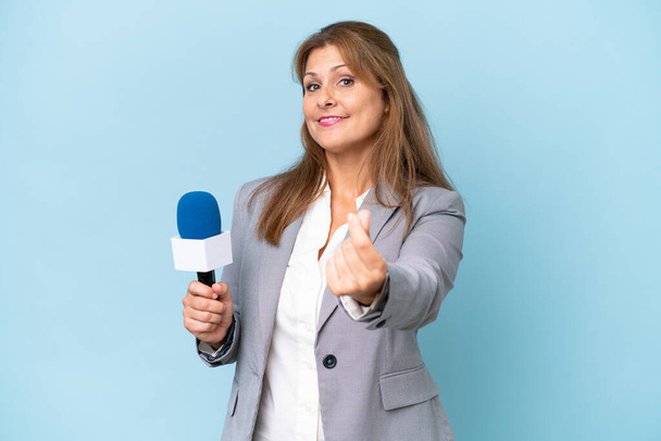 Mulher apresentadora de TV de meia-idade sobre fundo azul isolado fazendo gesto de dinheiro - Foto, Imagem