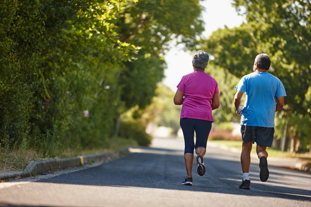 Garder les pieds en mouvement jusqu'à la retraite. Vue arrière prise d'un couple mature jogging ensemble par une journée ensoleillée - Photo, image