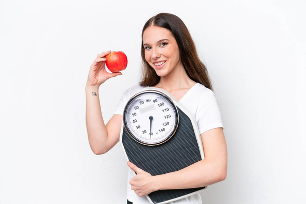Young caucasian woman isolated on white background with weighing machine and with an apple - Photo, Image