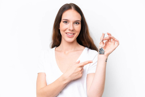 Young caucasian woman holding home keys isolated on white background and pointing it - Fotoğraf, Görsel