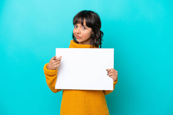 Young latin woman isolated on blue background holding an empty placard and pointing to the front - Photo, Image