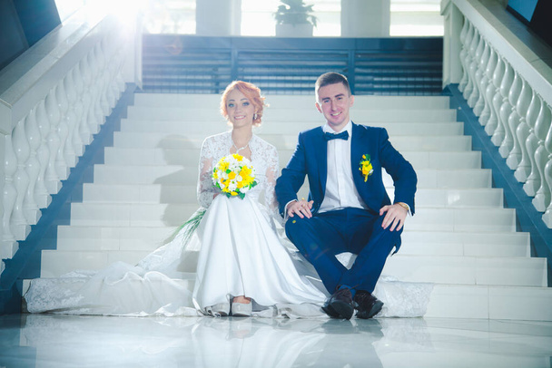 Mladý krásný pár v modrém obleku a bílé svatební šaty s kyticí v hotelu - Fotografie, Obrázek