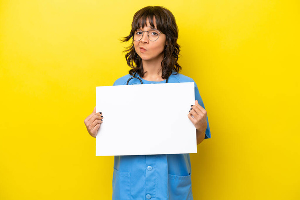 Sarı arka planda izole edilmiş genç bir hemşire kadın boş bir pankart tutuyor. - Fotoğraf, Görsel