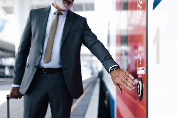 Позбавлення бізнесмена натискаючи кнопку відкритих дверей поїзда метро. Старший чоловік-професіонал стоїть на платформі. Він носить костюм під час ділових поїздок
. - Фото, зображення