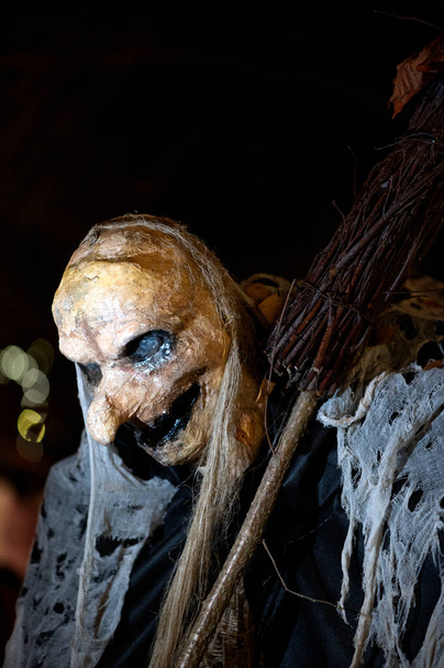 Bruja con una escoba y una cara de monstruo en una oscura noche de horror de Halloween, fondo claro bokeh - Foto, imagen
