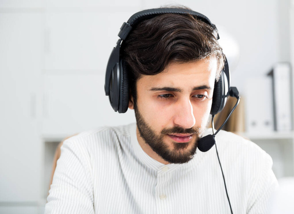 Smiling male business consultant with headphones sitting at deskin in office - Foto, Imagen