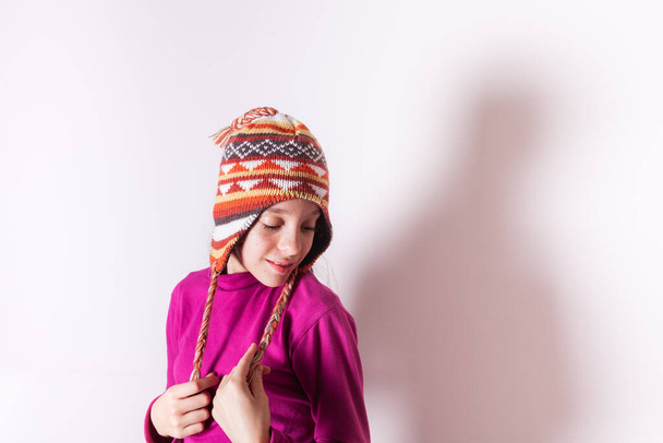 Petite fille portant un chapeau de laine souriant et regardant vers le bas sur fond blanc - Photo, image