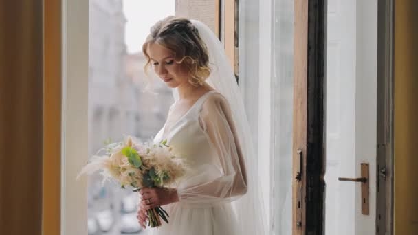 A menyasszony az ablakban egy csokor virággal. Az esküvője napján a menyasszony maga vizsgálja meg az esküvői csokrot. - Felvétel, videó
