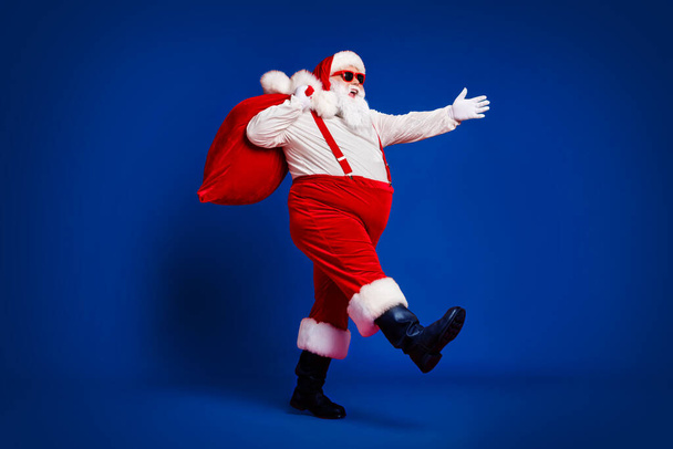 Full length body size view of his he attractive cheerful cheery funny fat Santa carrying big large sack delivery sale going isolated bright vivid shine vibrant red color background. - Фото, зображення