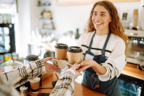 Smiling barista- girl giving take away coffee cups to a customers.   - Foto, Imagen