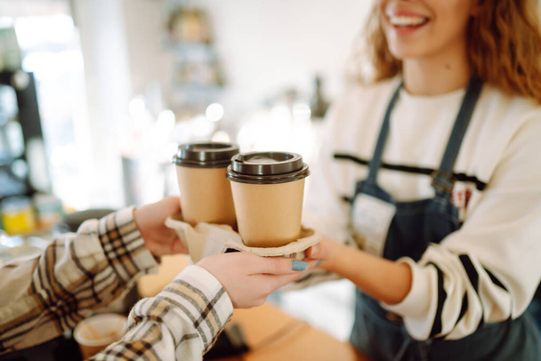 Smiling barista- girl giving take away coffee cups to a customers.   - 写真・画像