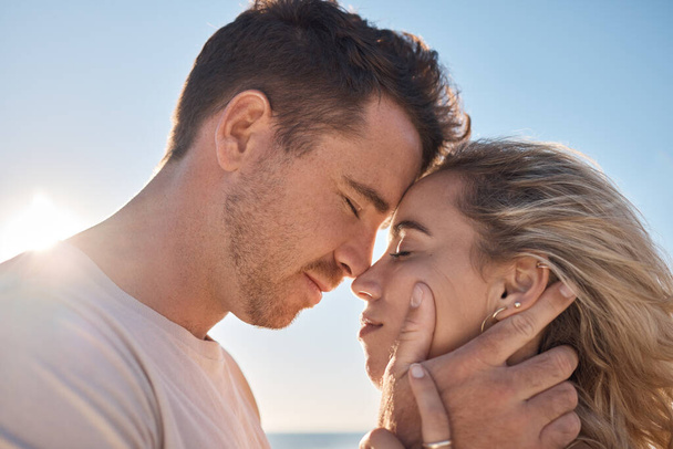 Couple, head touch and love at beach in closeup with romance, care and happiness for relationship. Man, woman and face together for care, bonding and together by ocean for vacation, holiday or summer. - Photo, Image