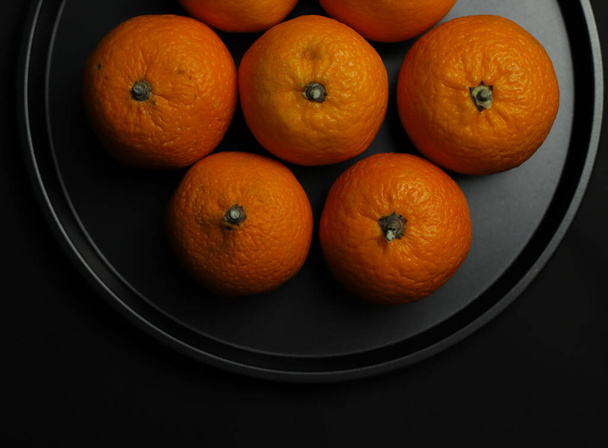 sweet orange round juicy whole tangerines lie on a black background round black tray.for postcards banners flyers invitations - Φωτογραφία, εικόνα
