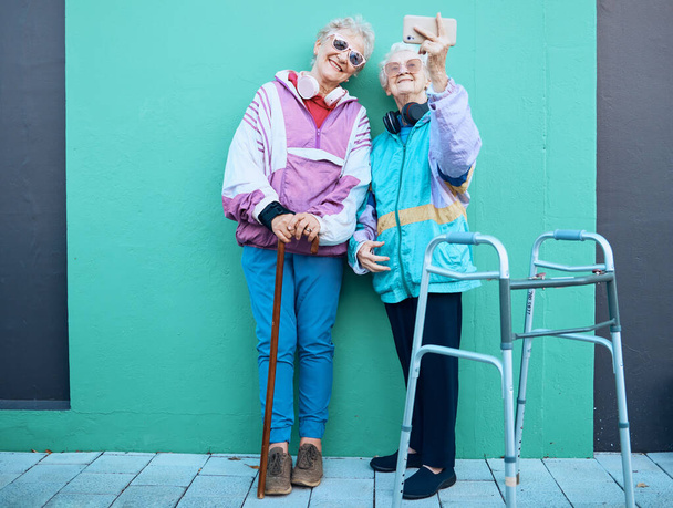 Telefone, selfie e deficiência com amigos seniores posando para uma fotografia ao ar livre em um fundo de parede verde. Feliz, móvel e caminhante com uma mulher madura e amiga tirando uma foto juntos. - Foto, Imagem