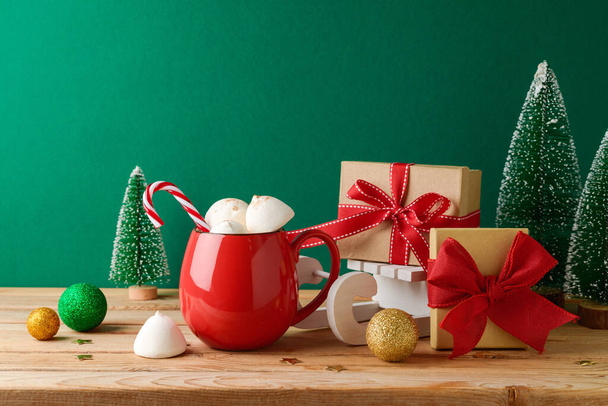 Christmas hot chocolate cup with marshmallow, gift boxes and decorations on wooden table over green background. Festive greeting card - Фото, зображення