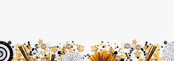 Yeni yıl arifesi altın ve siyah konfetilerden, gürültü çıkaranlardan, flamalardan ve dekorasyonlardan oluşan alt sınır. Beyaz afiş arkaplanındaki üst görünüm. - Fotoğraf, Görsel