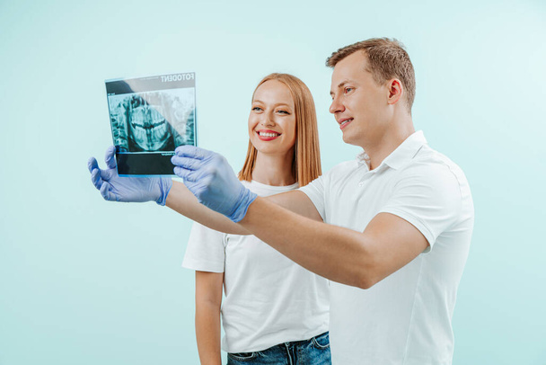 Doktor zubař a pacientka sledující rentgenové foto se zuby v světle modrém pozadí na zubní klinice. Úsměv zdravé zuby koncept - Fotografie, Obrázek