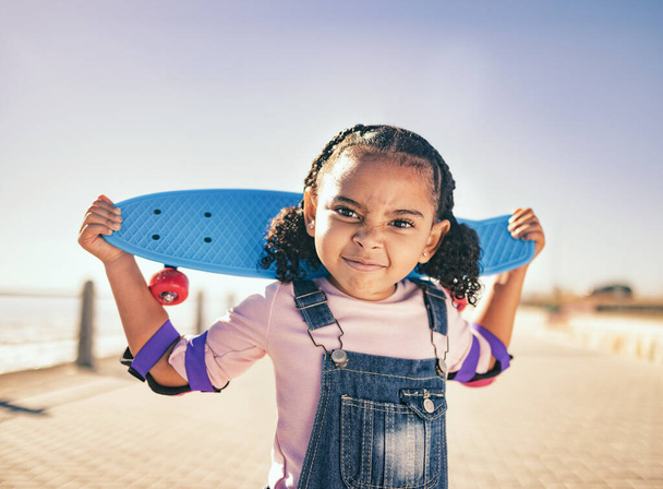 Skateboard, portrait et fille enfant à la promenade de la plage pour la pratique du patinage sur une promenade extérieure. Sport, entraînement et enfant avec visage comique pendant le skateboard au bord de l'océan en vacances au bord de la mer. - Photo, image