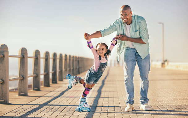 Skating, learning and father holding hands of his child while teaching her on the beach promenade. Family, love and dad helping his young girl kid for support, balance and care to outdoor rollerskate. - 写真・画像