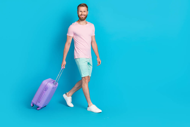 Full length photo of nice young guy baggage walking departure airport dressed stylish pink clothes isolated on aquamarine color background. - Foto, immagini