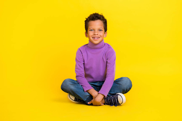 Full size photo of cheerful positive boy sit floor toothy smile good mood isolated on yellow color background. - Foto, afbeelding