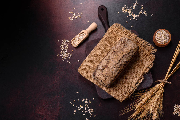 Una pagnotta di pane integrale con chicchi di cereali su un tagliere di legno su uno sfondo di cemento scuro - Foto, immagini