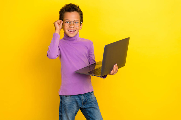 Photo of positive clever boy hand touch eyeglasses use wireless netbook isolated on yellow color background, - Fotografie, Obrázek