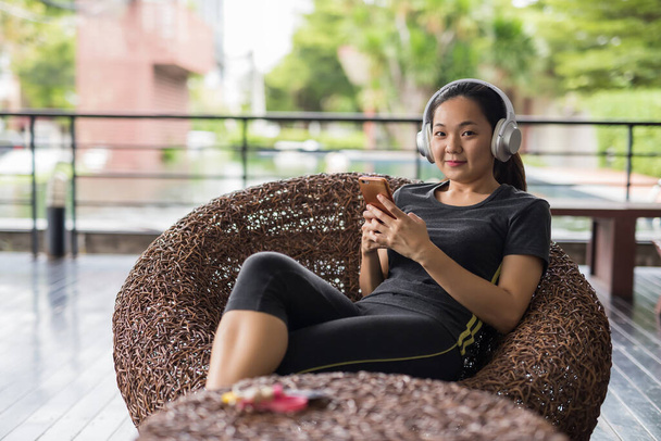 Молодая азиатская женщина пользуется смартфоном после тренировки или физических упражнений. Портрет здоровой девушки, заканчивающей фитнес-тренировку. - Фото, изображение