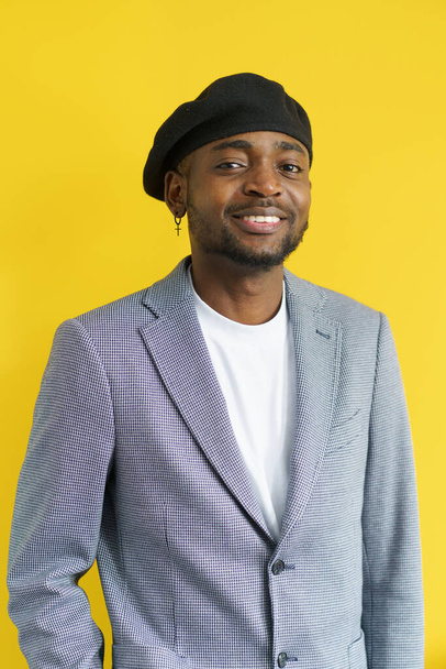 Happy handsome smiling to camera on yellow background. Young man in grey suit wearing black beret. Youth concept. High quality photo - Foto, Imagem