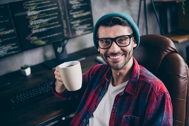 Photo of cheerful positive guy dressed eyewear enjoying tasty hot beverage indoors workstation workshop home. - Foto, imagen