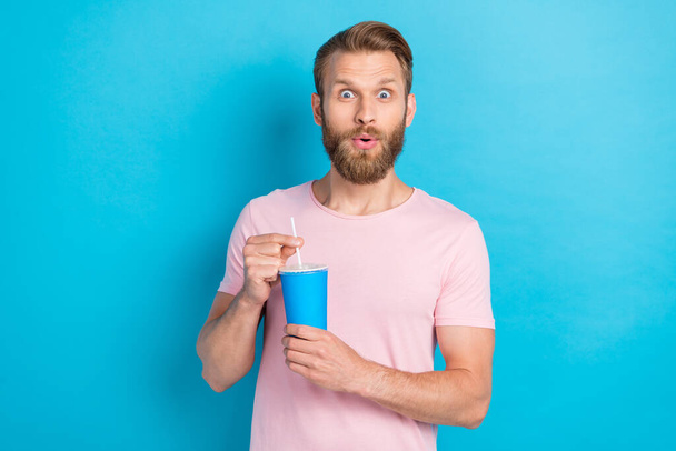 Photo of shocked impressed man wear pink t-shirt drinking cold soda big eyes isolated blue color background. - Fotografie, Obrázek