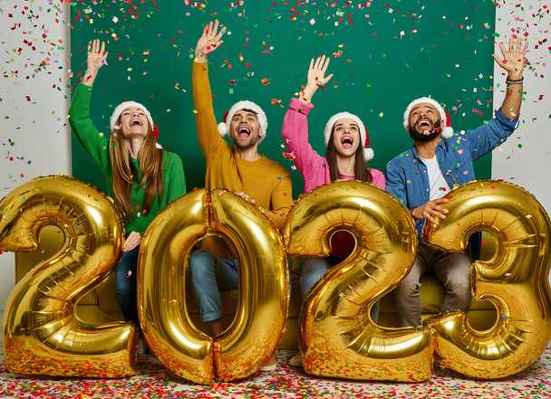 Studio shot of cheerful people carrying gold colored numbers and throwing confetti together - Foto, immagini