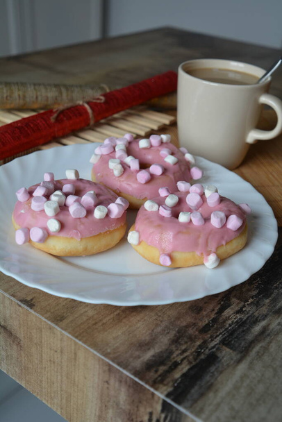 Cup of coffee with milk and three donuts with pink icing on a white plate. Sweet breakfast.  - Фото, зображення