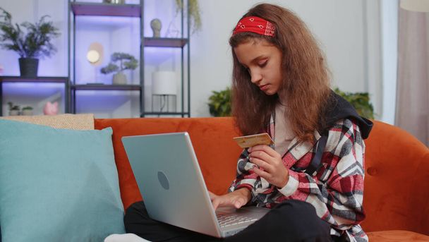 Portré egy kiskorú lányról, aki bankkártyát és laptopot használ, miközben pénzt utalgat, online vásárol, ételt rendel otthon. Fiatal tinédzser gyerek, gyerek a kanapén otthon szoba - Fotó, kép