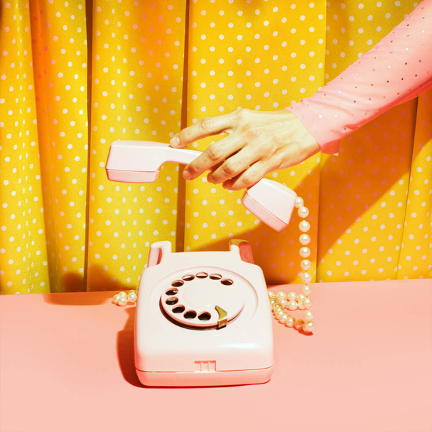 Old fashioned rotary dial telephone and female hand, creative nostalgic layout, retro aesthetic, pink and yellow background.  - Foto, Imagem