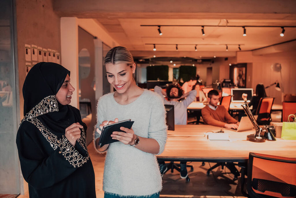A Muslim businesswoman woman and a young businesswoman in a modern office solve a problem together while using a tablet. High quality photo - 写真・画像