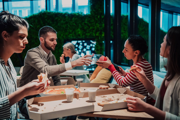 Харчуючись піцою з різноманітними колегами в офісі, щасливі багатоетнічні працівники розважаються разом під час обіду, насолоджуючись гарною розмовою та емоціями
. - Фото, зображення