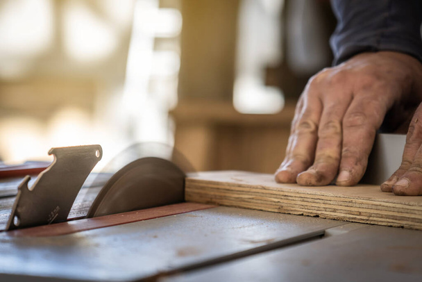 Primer plano de las manos de un carpintero cortando madera con una sierra circular. - Foto, Imagen