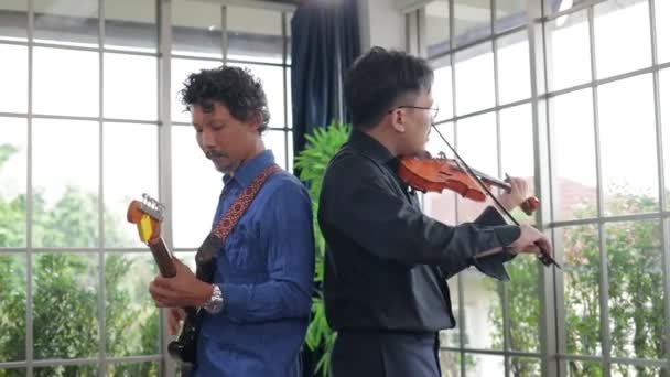 İki Asyalı müzisyen pratik odasında klasik enstrüman, keman ve elektro gitar çalıyor. Canlı müzik ve bando çalma kavramı. Kayıt stüdyosunda müzik çalıyor.. - Video, Çekim