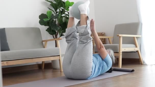 Asiática anciana haciendo ejercicio en casa con bola de yoga Hacer una posición de elevación de la ingle en la pelota. aumentar la flexibilidad del cuerpo Reducir el dolor de espalda. concepto de asistencia sanitaria en la jubilación - Metraje, vídeo