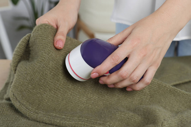 Woman cleaning clothes with fabric shaver indoors, closeup - Foto, imagen